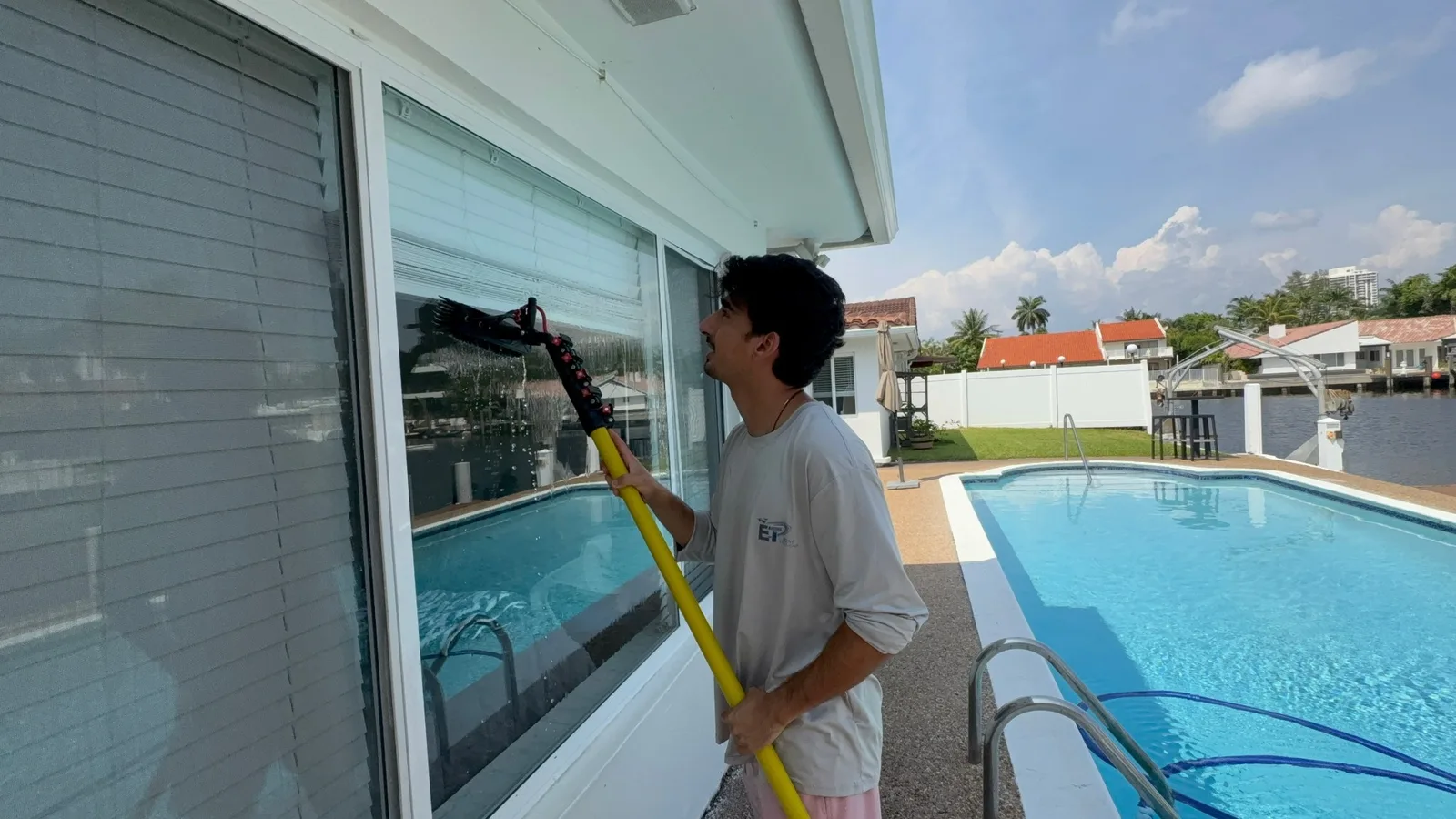 ET Drone Solutions technician cleaning a window with a water fed pole beside a pool